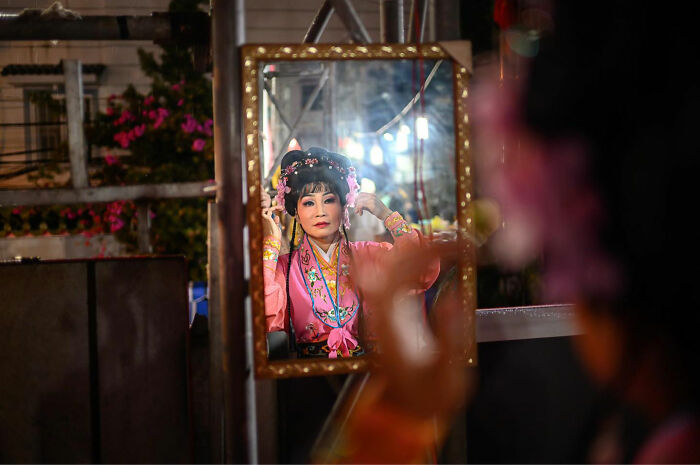 Woman in traditional Asian costume adjusting hair in mirror, one of the candid everyday moments from Asia by photographer Gil Kreslavsky.