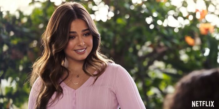 Young woman in a pink top smiling outdoors with blurred greenery in the background in a Netflix movie scene about letdowns