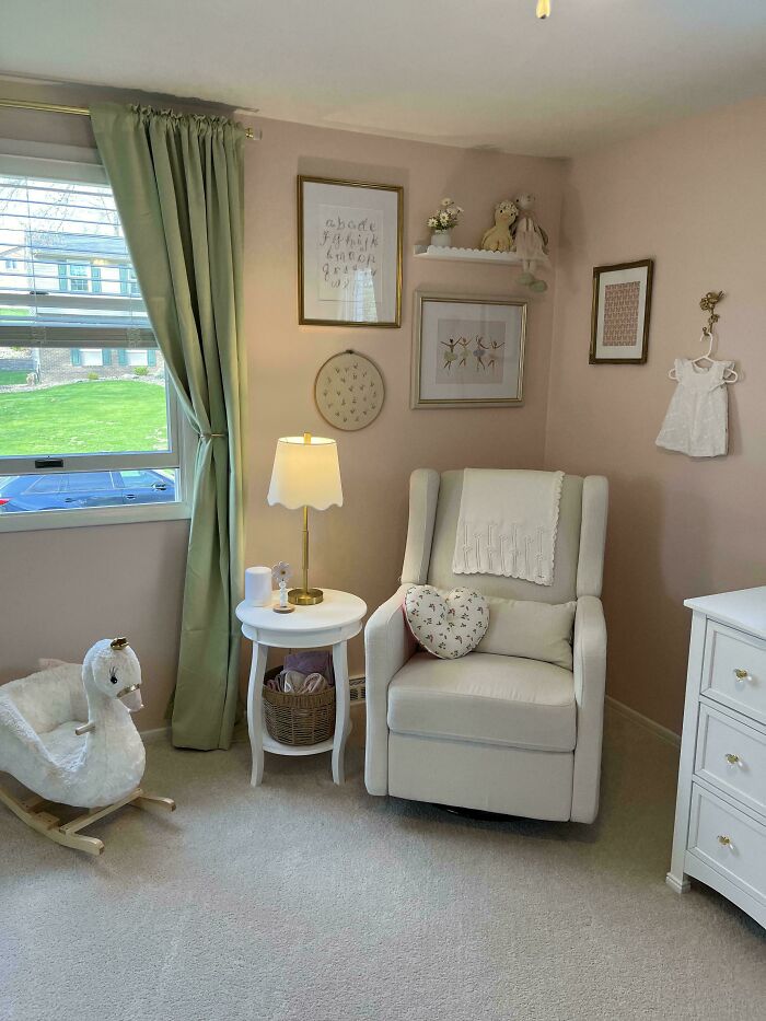 Cozy corner of a home decorated with a white armchair, heart pillow, lamp on side table, and playful nursery wall art.