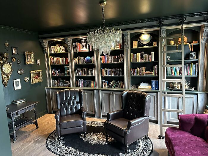 Cozy home library with dark walls, leather armchairs, chandelier, and built-in bookshelves showcasing a stylish home decoration.