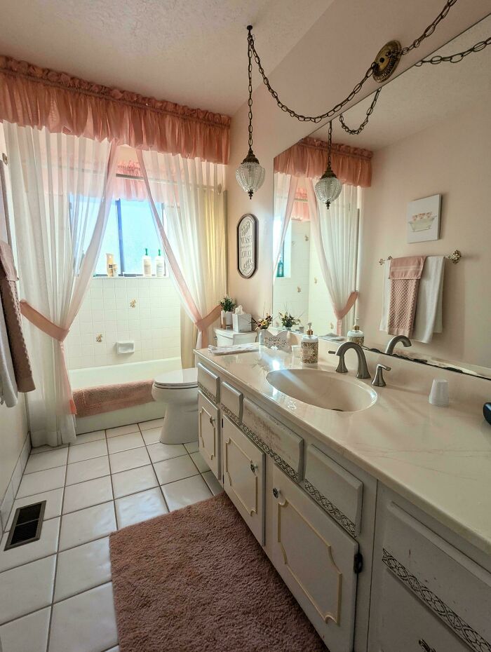 Bathroom with elegant home decoration featuring vintage lighting, pink curtains, and a neatly arranged vanity area.