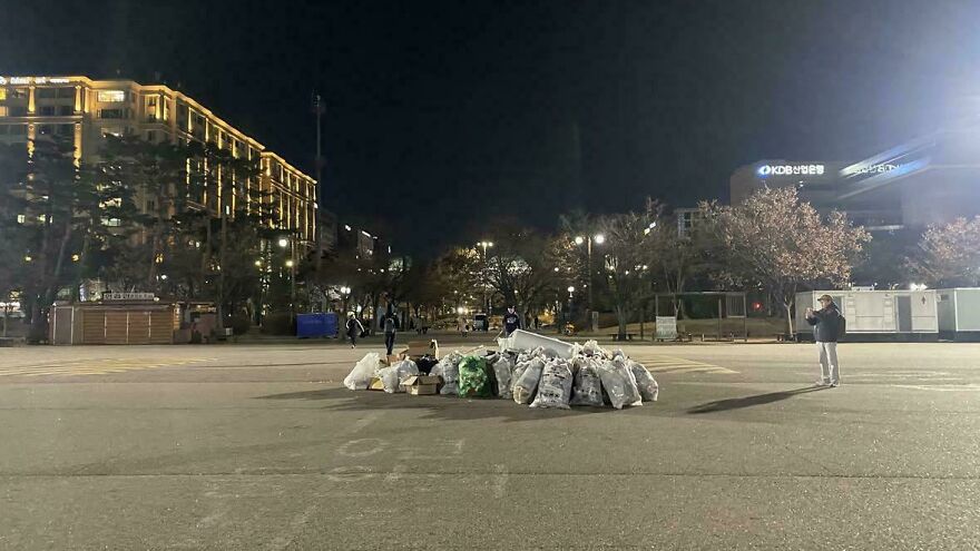 Nighttime view of an open area with piles of bags and people in the distance, showcasing interesting community cleanup efforts