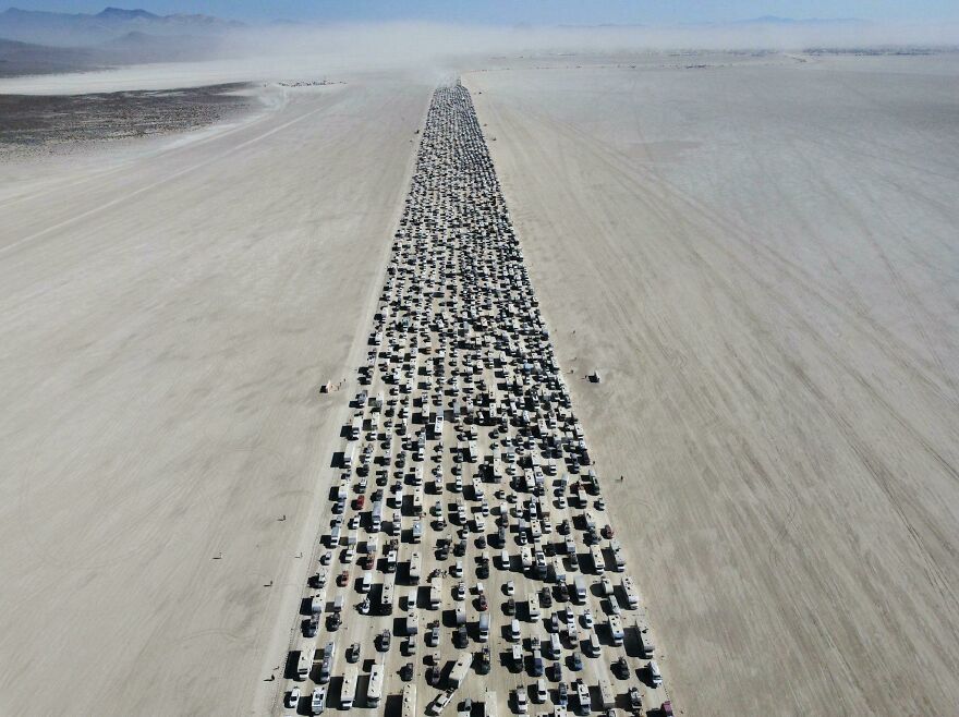 Aerial view of a massive gathering with hundreds of vehicles lined up in a desert, showcasing an interesting online community event.