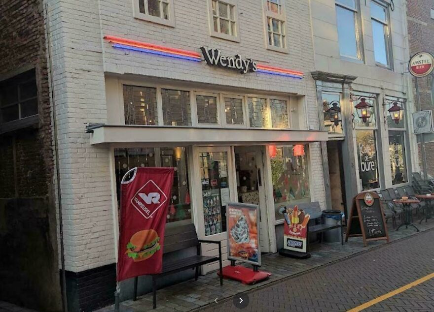 Wendy's fast food restaurant exterior with promotional banners and outdoor seating on a city street view.