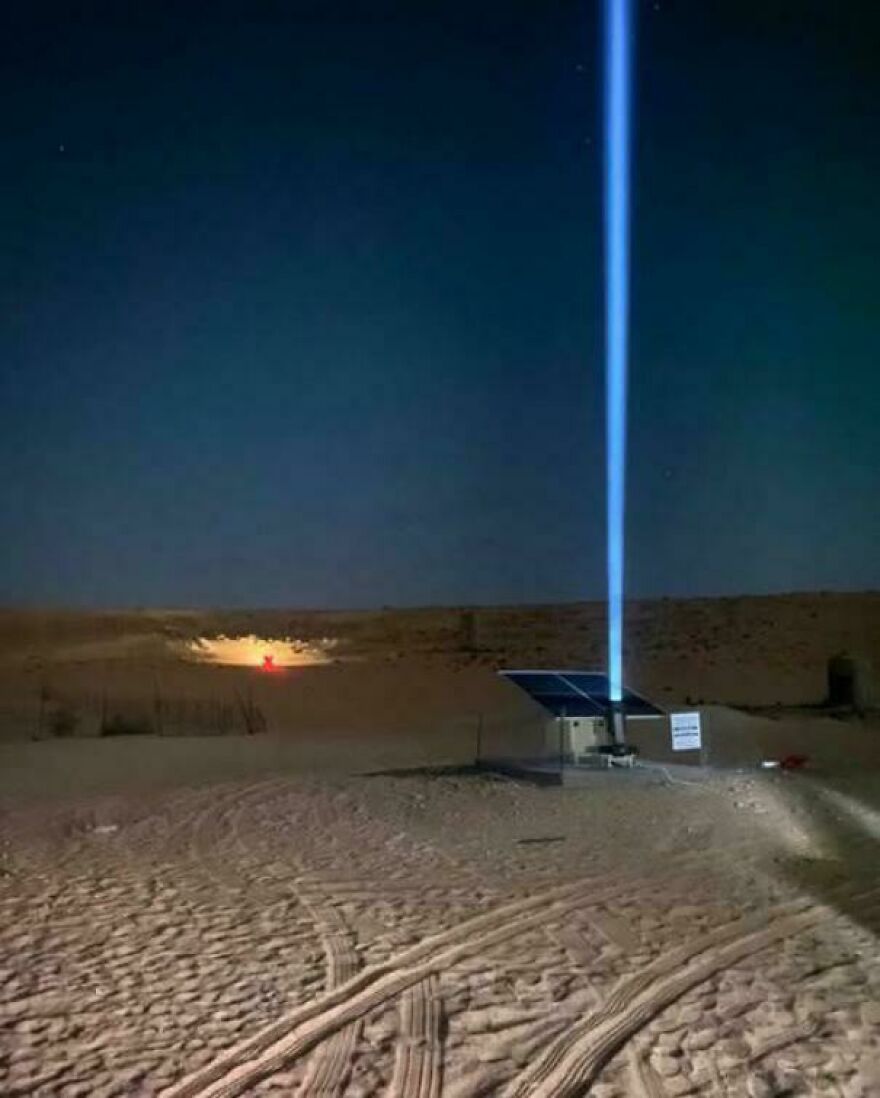 Bright blue laser beam shooting into the night sky from solar panels in a desert, showcasing an interesting technology post.