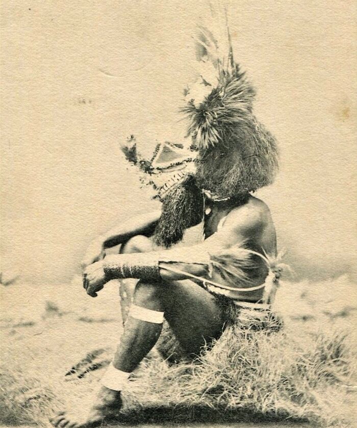 Indigenous Australian man from the 1900s wearing traditional ceremonial attire and headgear, captured in a historic photo.