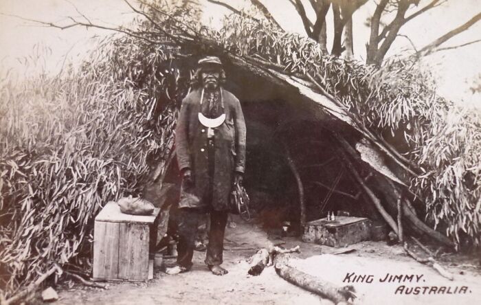 Indigenous Australian man standing outside traditional shelter, offering rare glimpses into 1900s Indigenous Australians life.