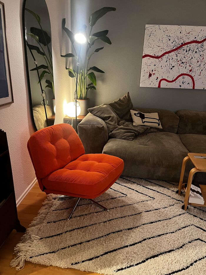 Cozy home corner featuring a bright orange chair, green couch, modern art, and ambient lighting, showcasing proud home decorating.