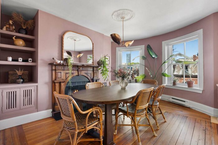 Cozy dining room corner with wooden table, wicker chairs, fireplace, and decorative plants in a beautifully decorated home.