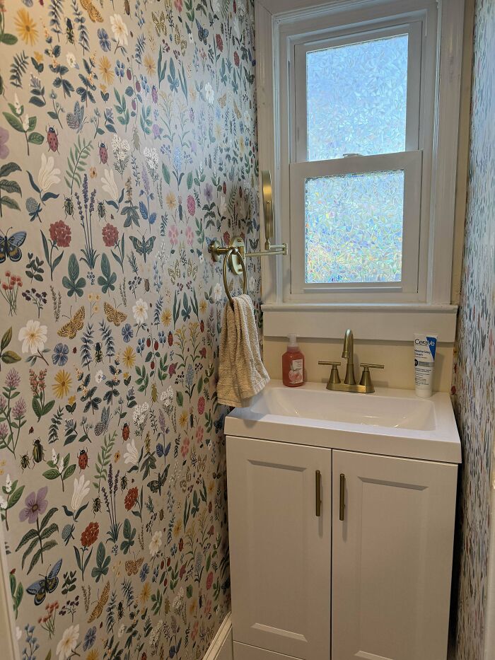 Small bathroom corner with floral wallpaper, white sink cabinet, gold fixtures, and frosted window showcasing home decoration pride.