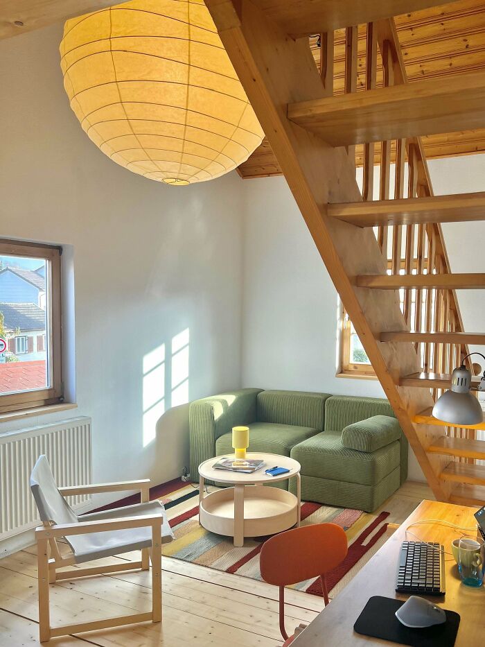 Cozy corner of a home featuring a green sofa, wooden staircase, round coffee table, and natural light from a window.