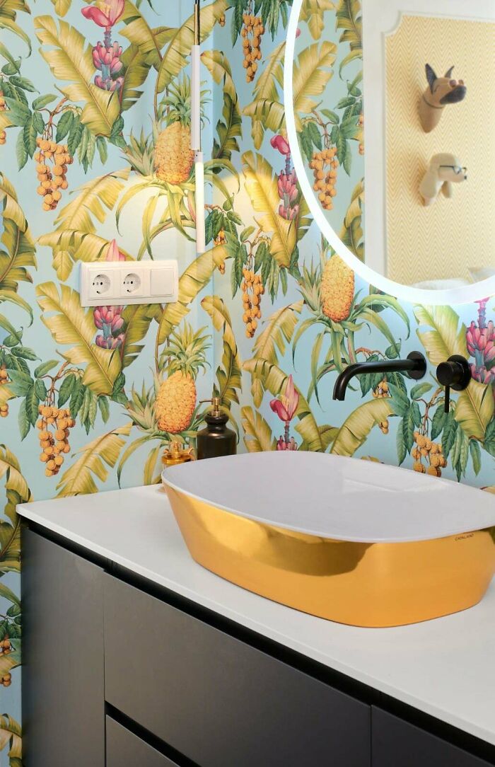 Bathroom corner featuring tropical wallpaper and a gold sink, showcasing a unique home decorating detail.