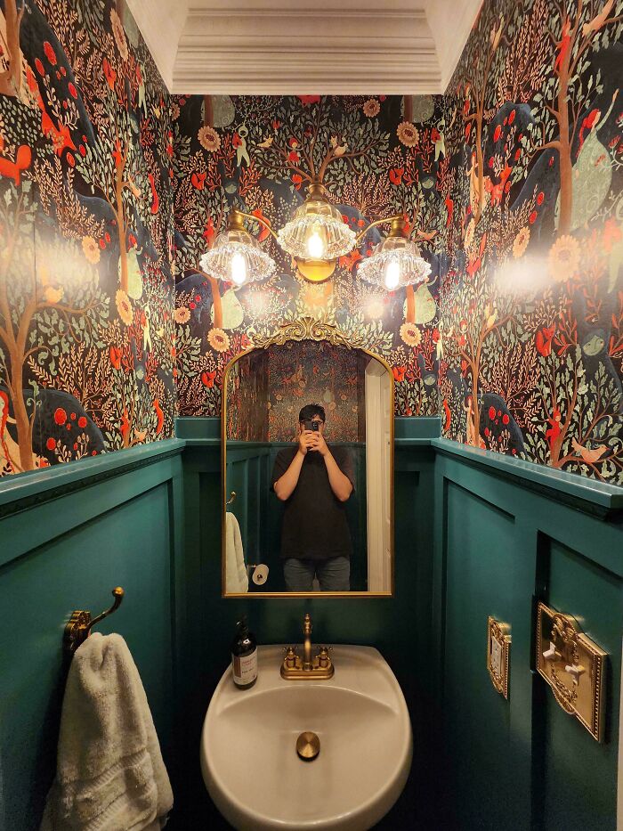 Bathroom corner with vibrant floral wallpaper, vintage lighting, and decorative mirror showcasing home decorating pride.