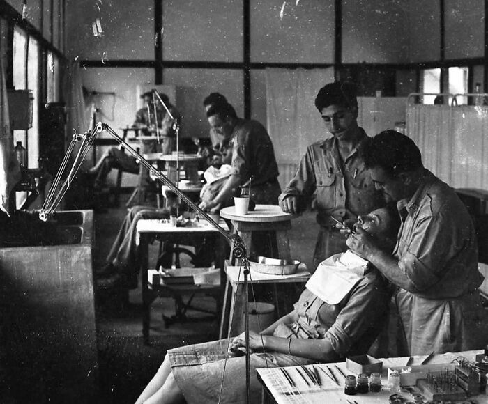 Black and white rare WWII photo showing military personnel receiving dental care in a makeshift wartime clinic.