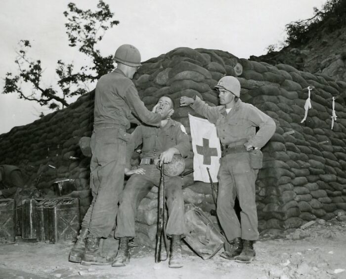 WWII rare photo showing soldiers at a sandbag bunker with a medical aid flag and soldier receiving treatment.