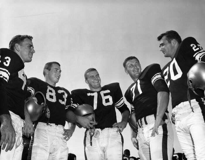 1950s Florida football players in vintage uniforms smiling and standing together during a sunny day practice session.