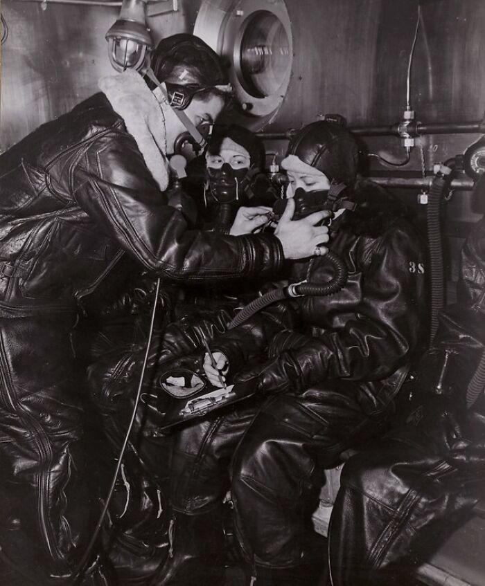 Three WWII airmen in leather flight gear wearing oxygen masks inside a military aircraft, a rare WWII photo from the era.