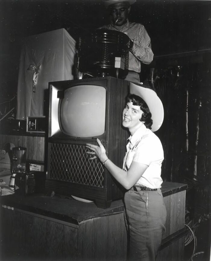 Woman in a cowboy hat smiling and posing with a vintage television in everyday life in 1950s Florida.