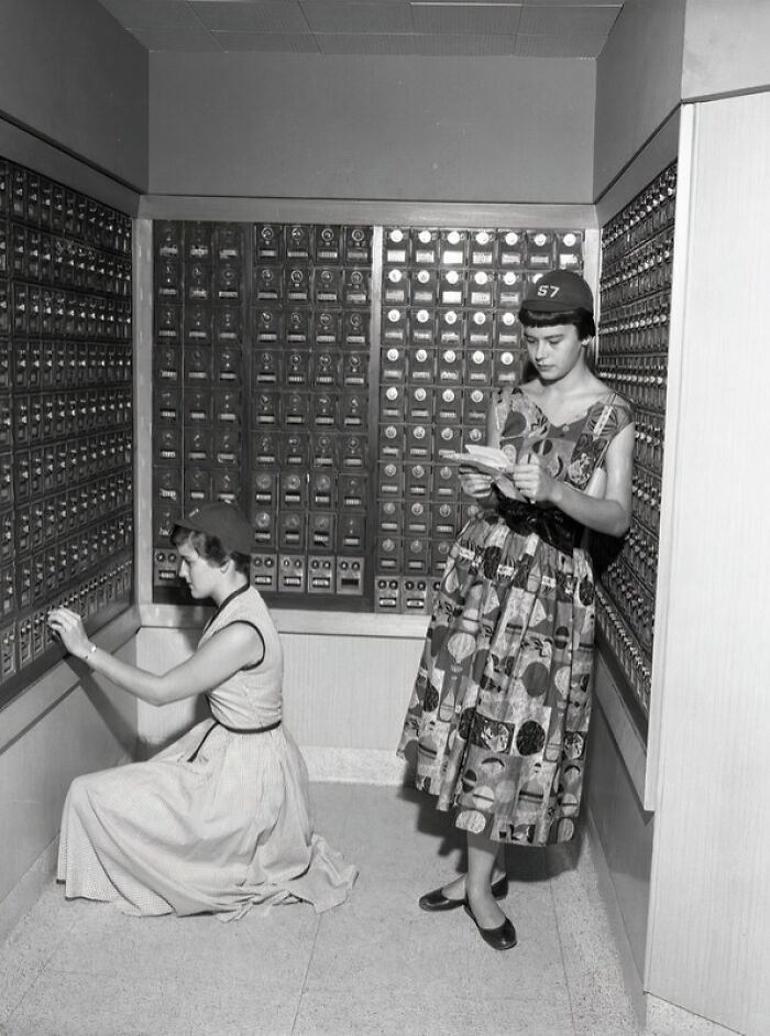 Two women in 1950s dresses checking mailboxes in a post office, iconic glimpses into everyday life in 1950s Florida.