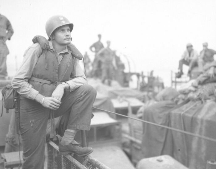World War II soldier wearing helmet and life vest, standing on a military ship in a rare WWII photo.