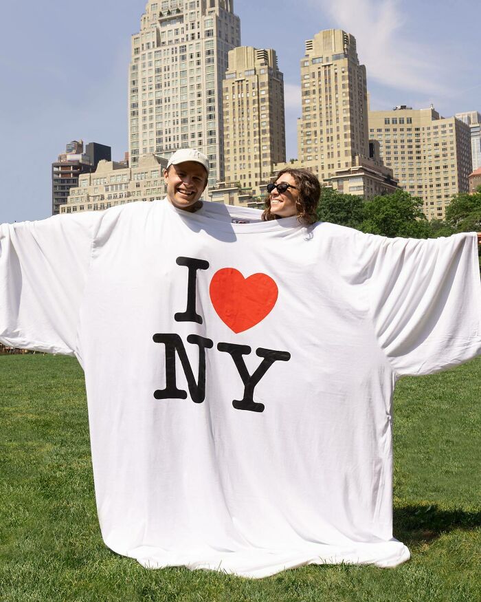 Two people wearing an oversized I Love NY shirt, showcasing unusual accessories by Nik Bentel blending everyday objects with fashion.