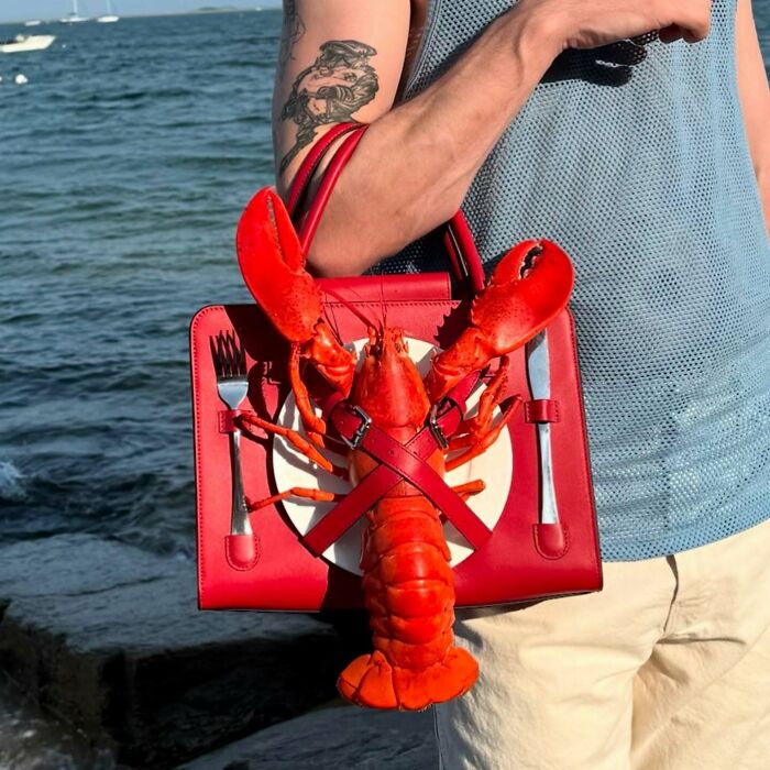 Man holding a red fashion accessory bag featuring a lobster and cutlery blending everyday objects with fashion design.