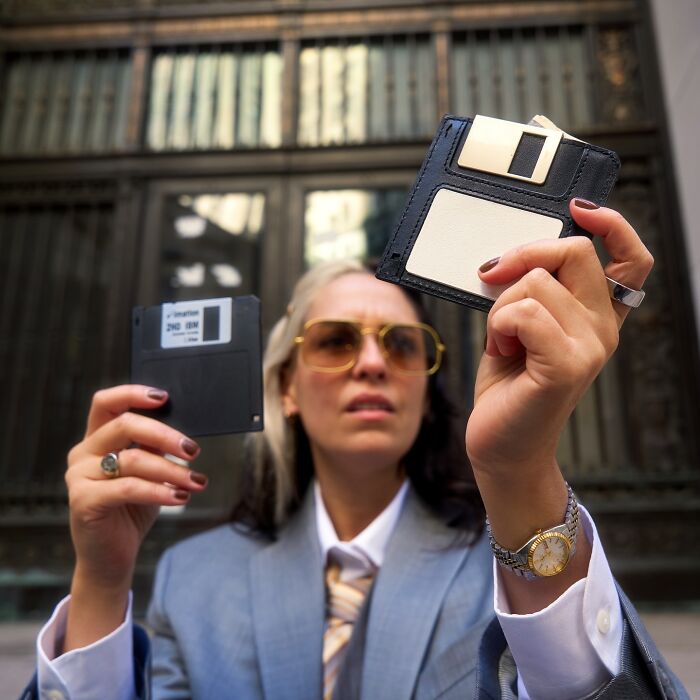 Person holding a floppy disk and a fashion accessory inspired by a floppy disk, showcasing unusual accessories by Nik Bentel.