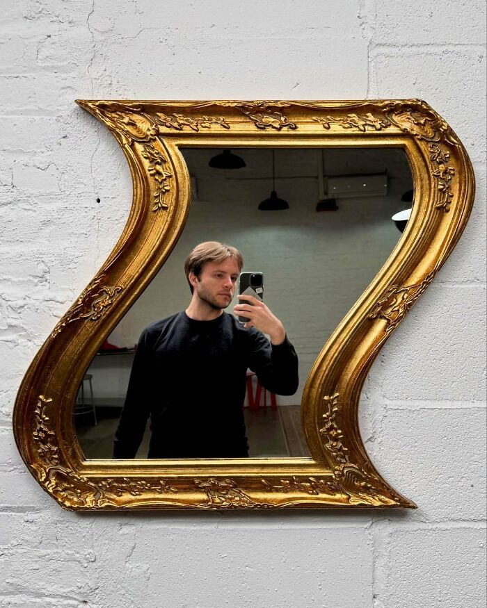 Man taking selfie in a uniquely shaped decorative mirror, showcasing unusual accessories blending everyday objects with fashion.