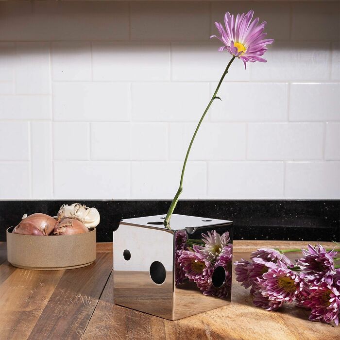 Reflective cube vase blending everyday objects with fashion, holding a single purple flower on a wooden kitchen countertop.