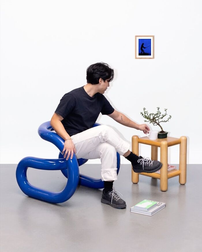 Person sitting in a blue sculptural chair reaching for a cup on a wooden side table with a plant, showcasing unusual accessories.