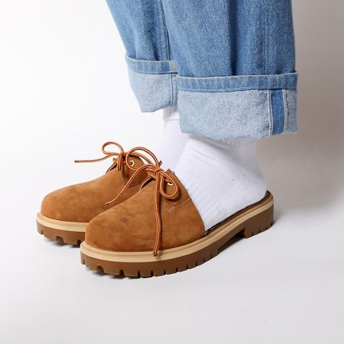 Brown suede shoes with thick rubber soles worn with white socks and rolled-up jeans, showcasing unusual fashion accessories.