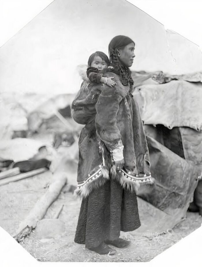 Inuit woman carrying a child on her back, dressed in traditional fur clothing, showcasing the unbreakable spirit of the Inuit.