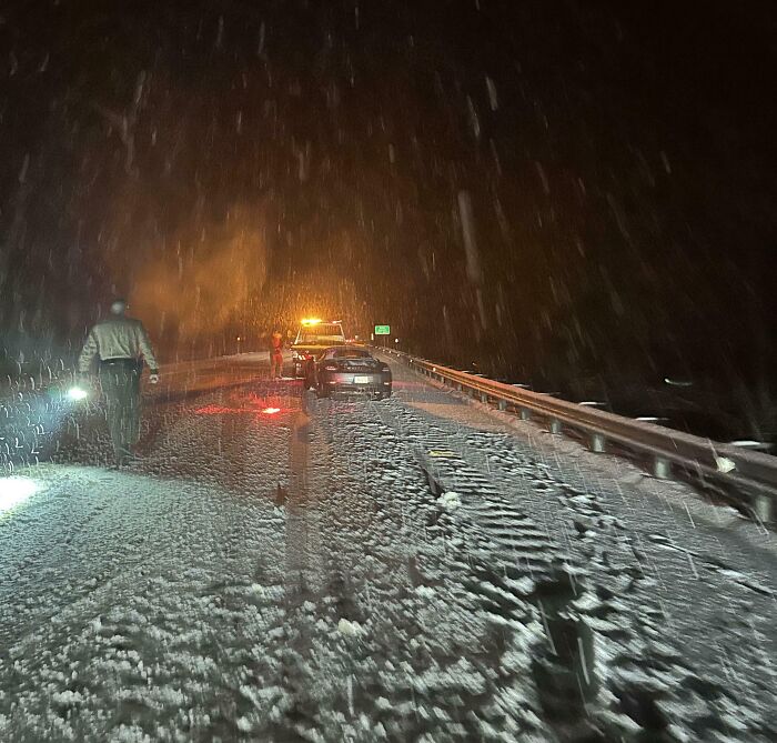Police and tow truck on a snowy road at night during a wild Mother Nature storm with heavy snowfall and low visibility.