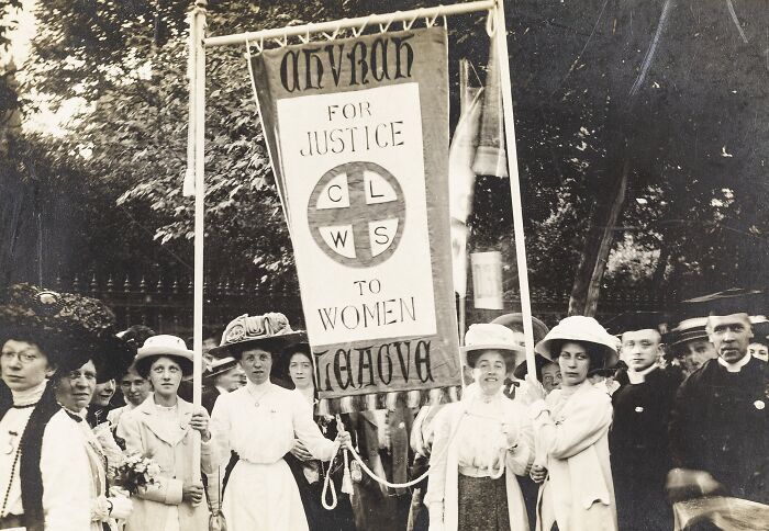 Women in the 20th century suffrage era holding a banner demanding justice and voting rights in a historic protest.
