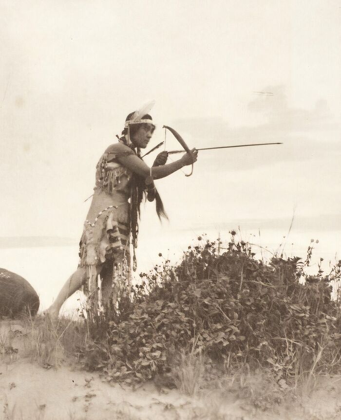 Native tribes strength captured in 1900s photo showing a man aiming a bow and arrow in traditional attire.