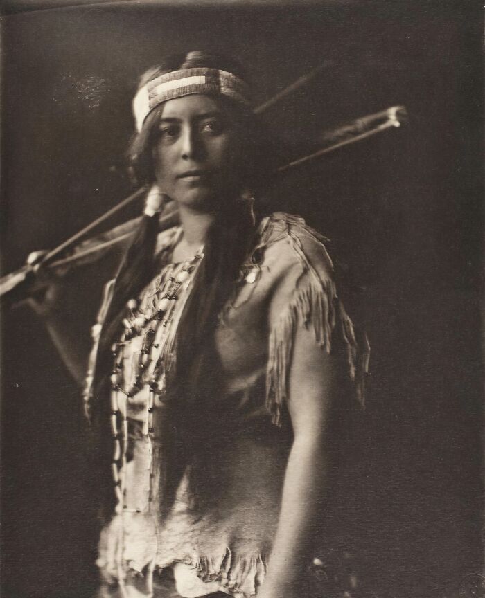 Native tribeswoman in traditional attire holding a spear, captured in a powerful 1900s portrait by a photographer.