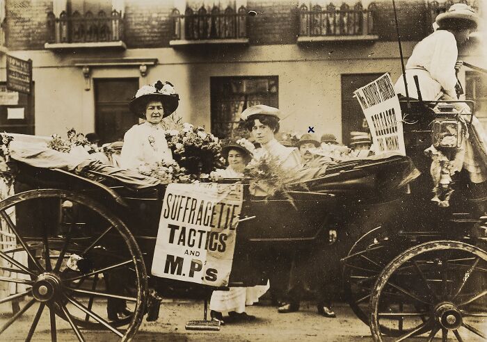 Women in the 20th century suffrage era riding a horse-drawn carriage with protest signs for voting rights.