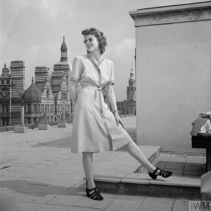 British woman in stylish WWII era dress and sunglasses posing on a rooftop, showcasing fashion during WWII restrictions.