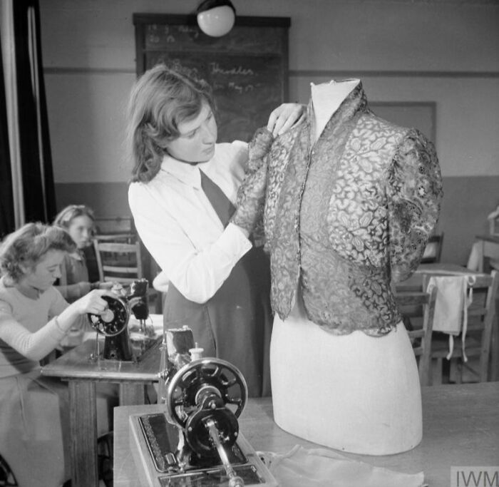 British women maintaining style during WWII restrictions, tailoring a vintage jacket on a mannequin in a sewing room.