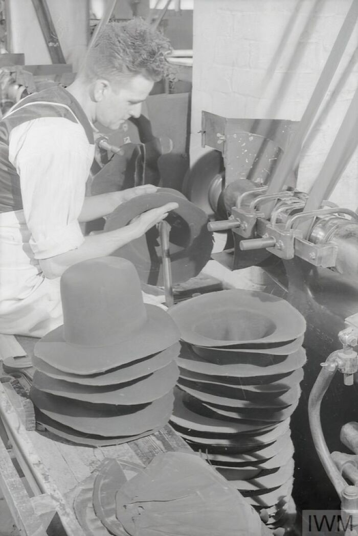 Man shaping hat brims by machine in factory, illustrating British women style adaptation during WWII restrictions.
