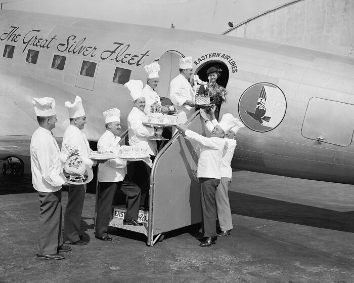 Chefs dressed in white uniforms serving food on a glamorous Eastern Air Lines vintage airplane flight.