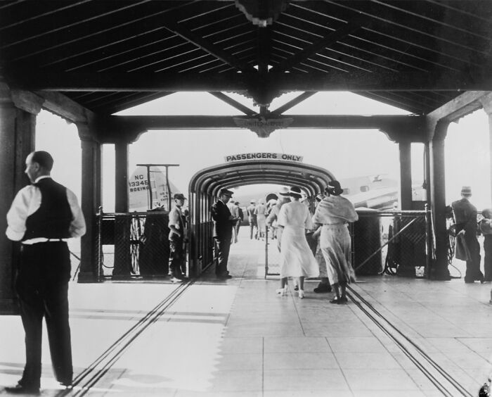 Passengers dressed in elegant attire walking through a vintage airport terminal, showcasing flying as an affair of pure glamour.