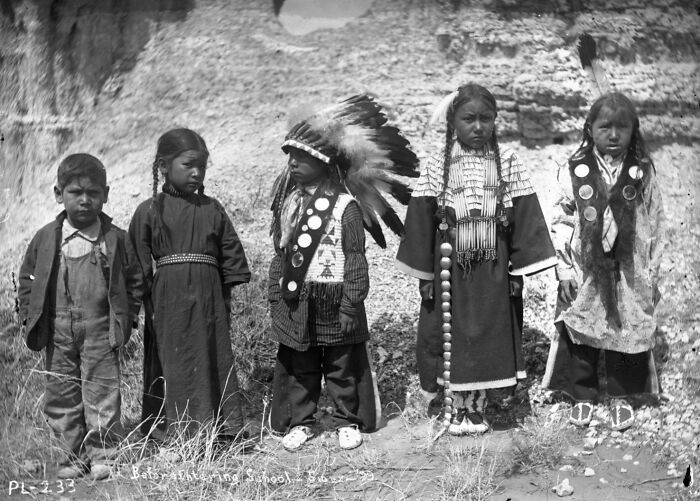 Five Native American children in traditional and school attire at a boarding school in the 1910s, historical photo.