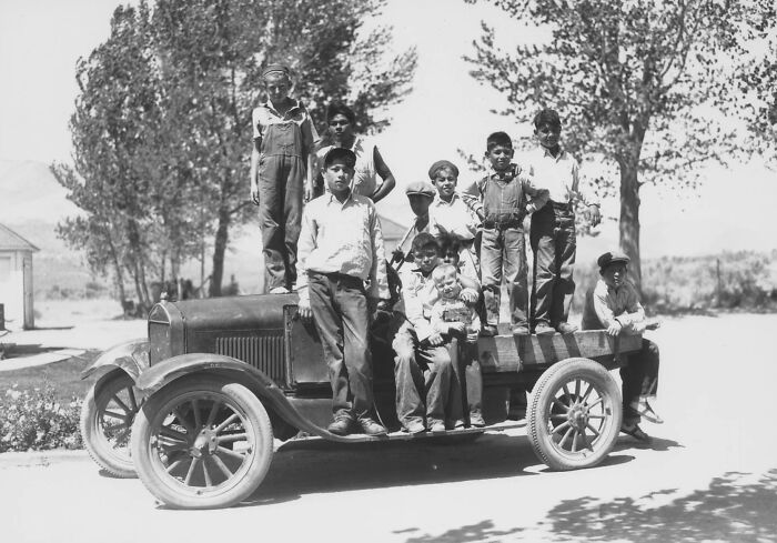 Group of Native American boys from boarding schools in the 1910s standing and sitting on an old truck outdoors.