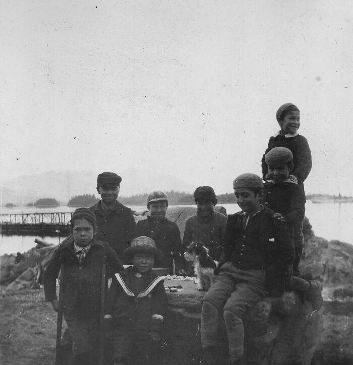 Black and white photo of Native American children at a boarding school outdoors by water in the 1910s era.