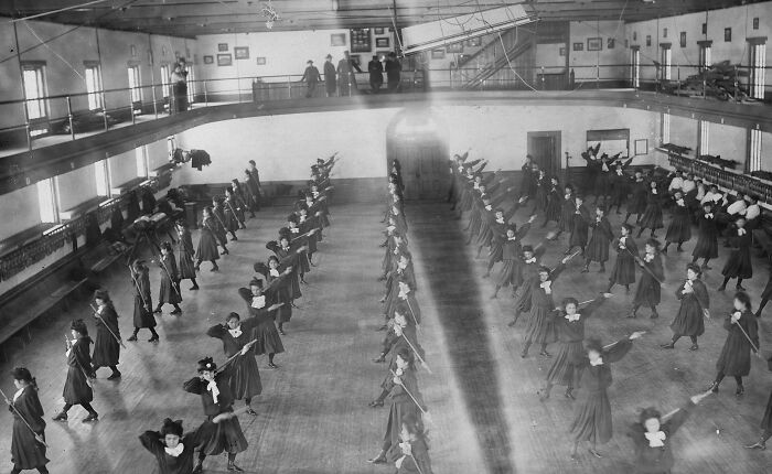 Native American boarding school students in the 1910s practicing drills inside a large gymnasium hall.