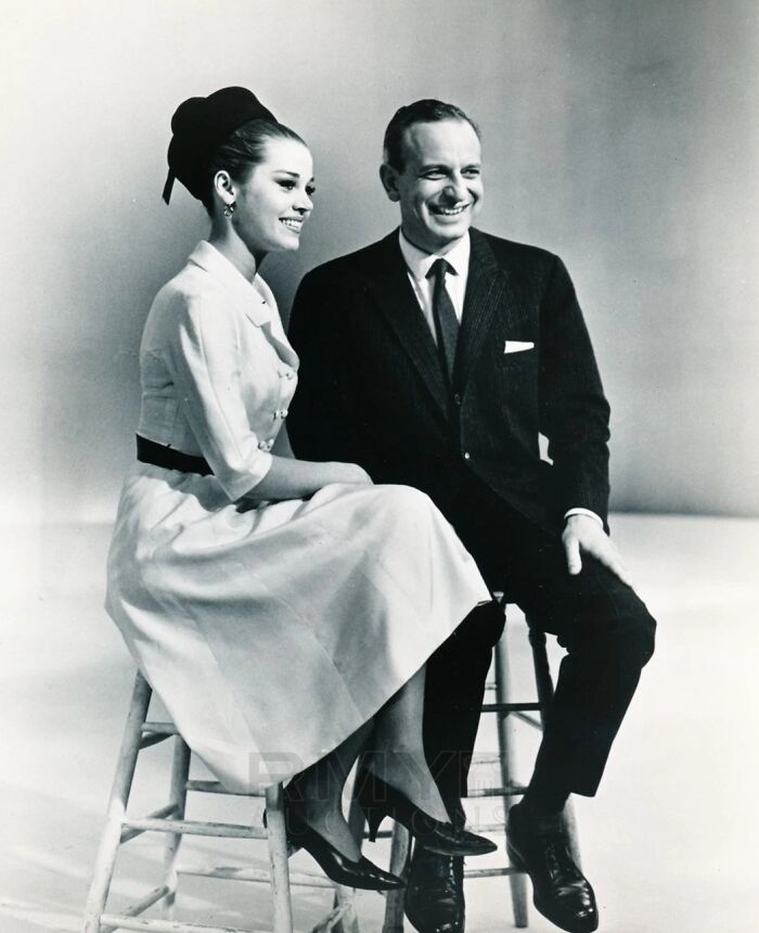 LA woman in a 1960s dress sitting beside a man in a suit, both smiling and enjoying a casual moment together.