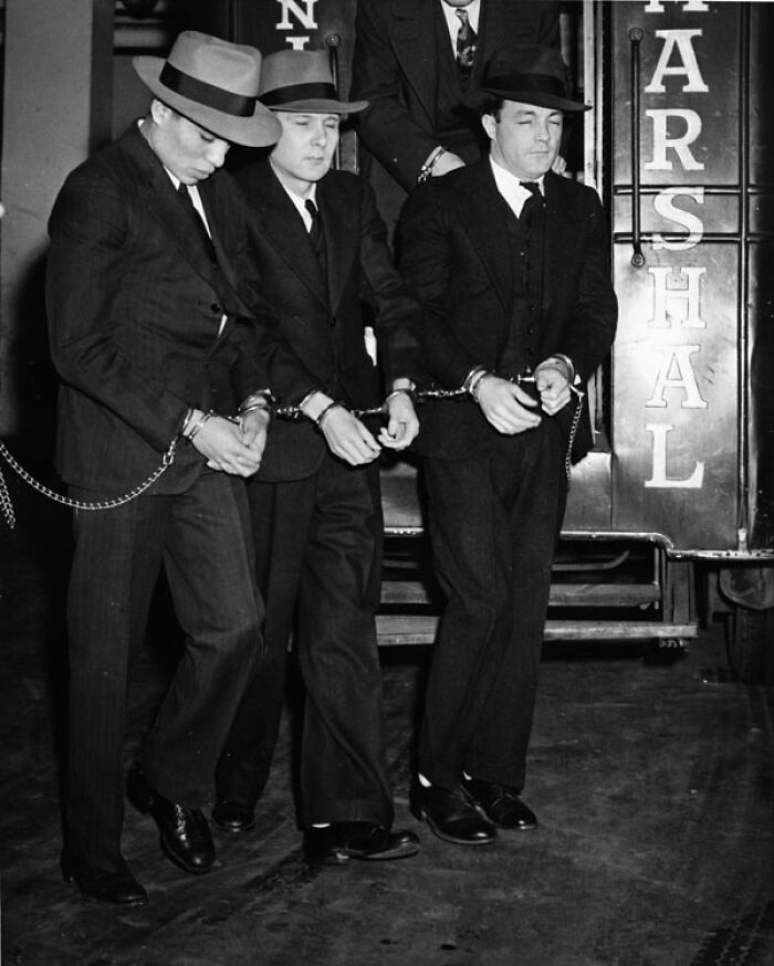 Three men in handcuffs and suits, escorted by a marshal, showing harsh reality of life on Alcatraz.