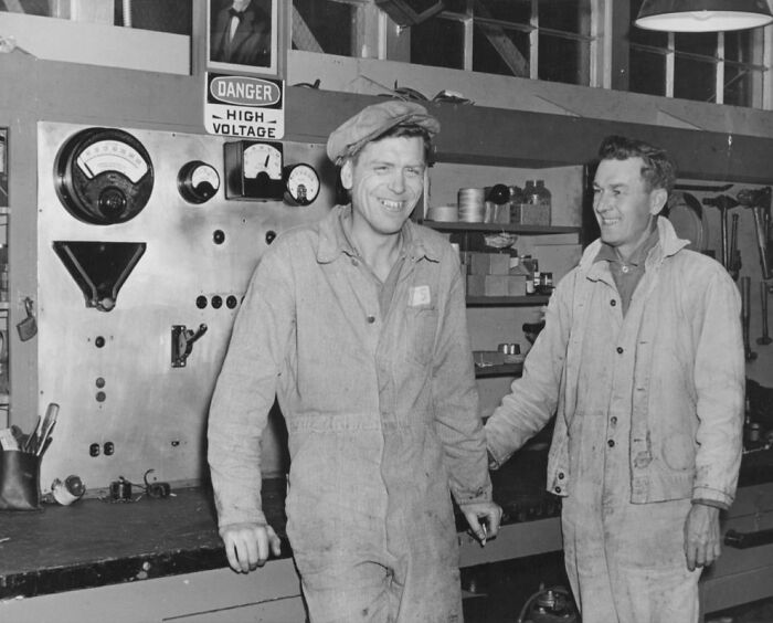 Two men in workwear standing and smiling inside an industrial setting, showing rare glimpses into life on Alcatraz.