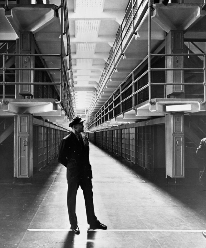 Black and white photo of a guard standing inside Alcatraz prison hallway, showcasing harsh reality of life on Alcatraz.